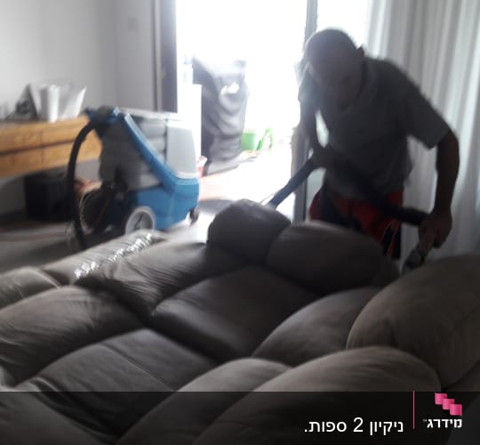 אדם מנקה ספה עם שואב אבק מקצועי